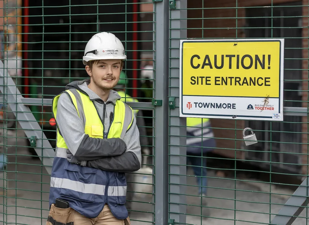 Townmore worker leaning against fence with a caution sign on it