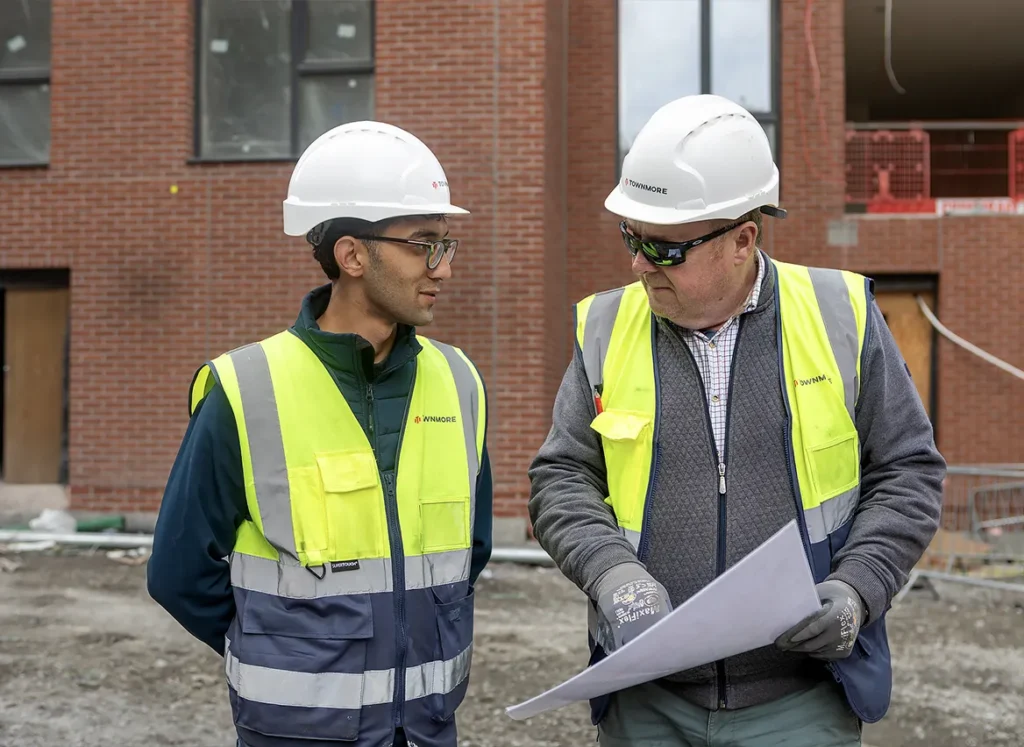Two men looking at paper plans wearing construction gear